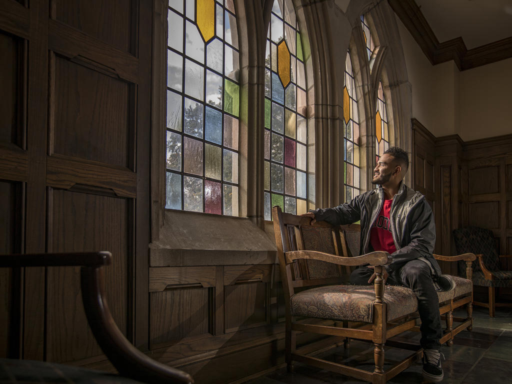 a young African American man looks outs a stained glass window