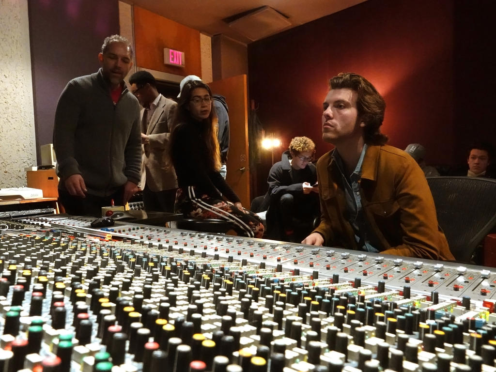 A person in a leather jacket sits in front of a sound board