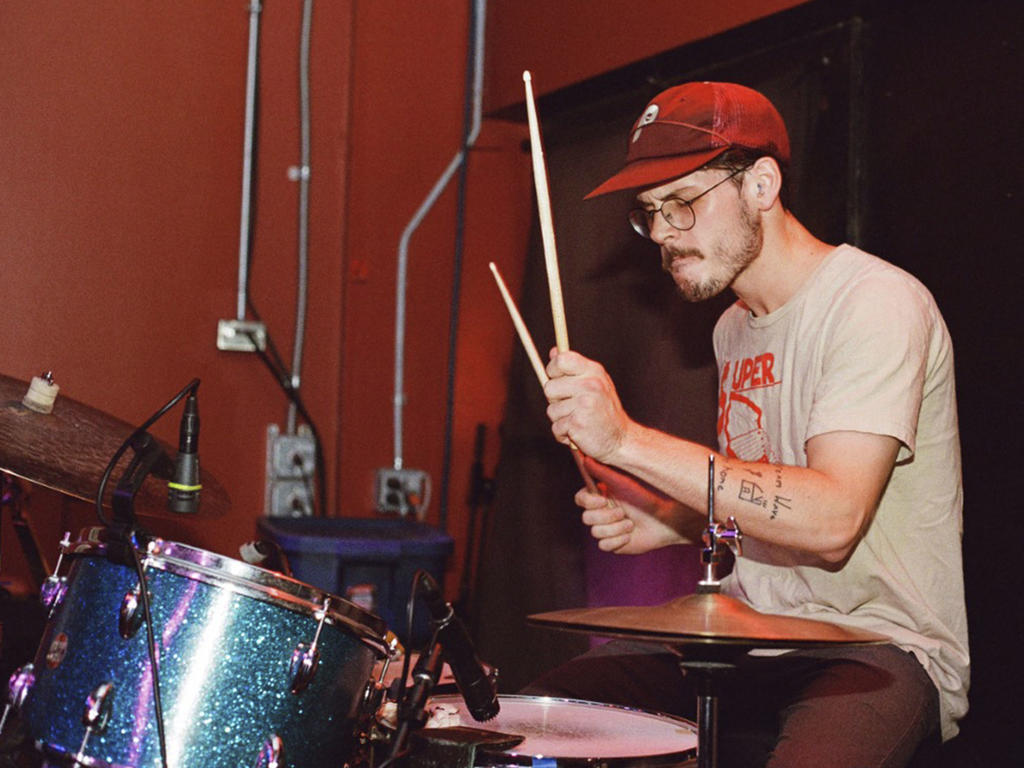a young man in a baseball hat plays the drums