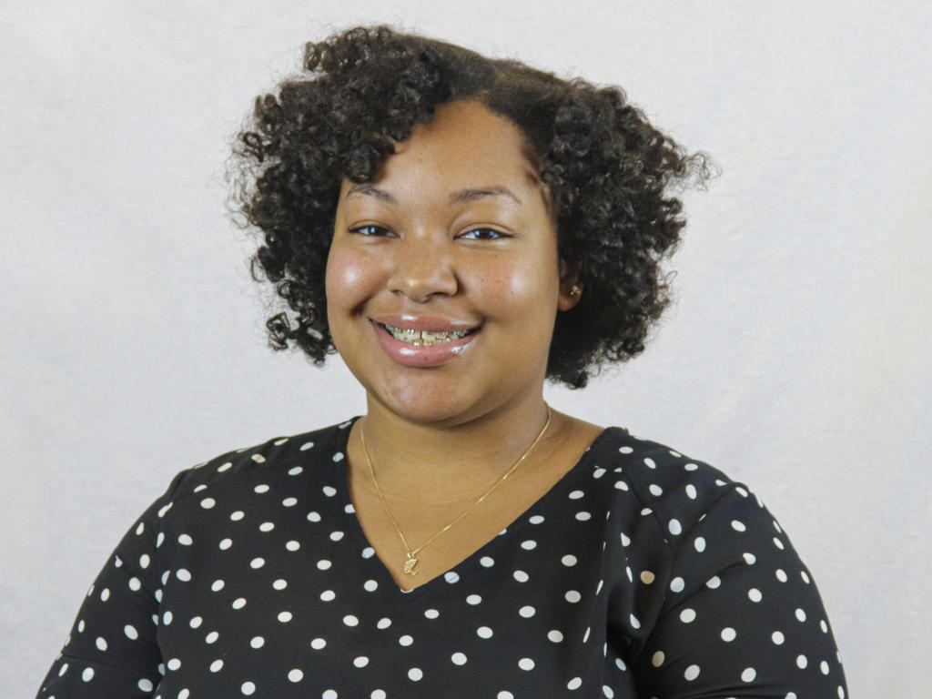 a young African American woman in a polka dot top smiles at the camers