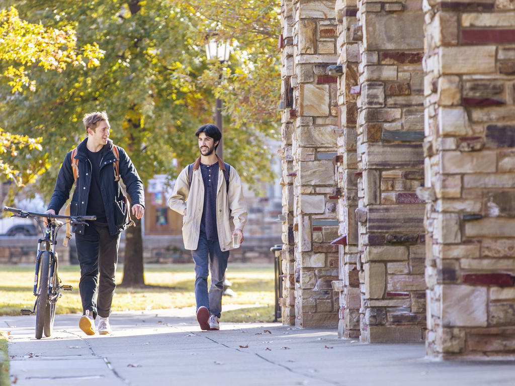 One person with bike walks down stone arch-lined path with another person