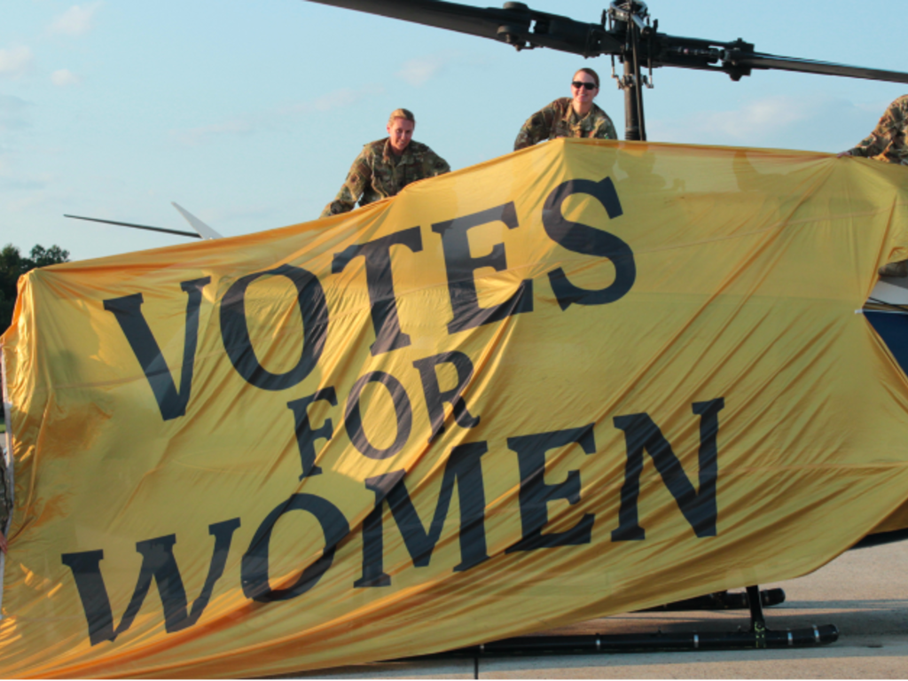 women in uniform hold up a banner
