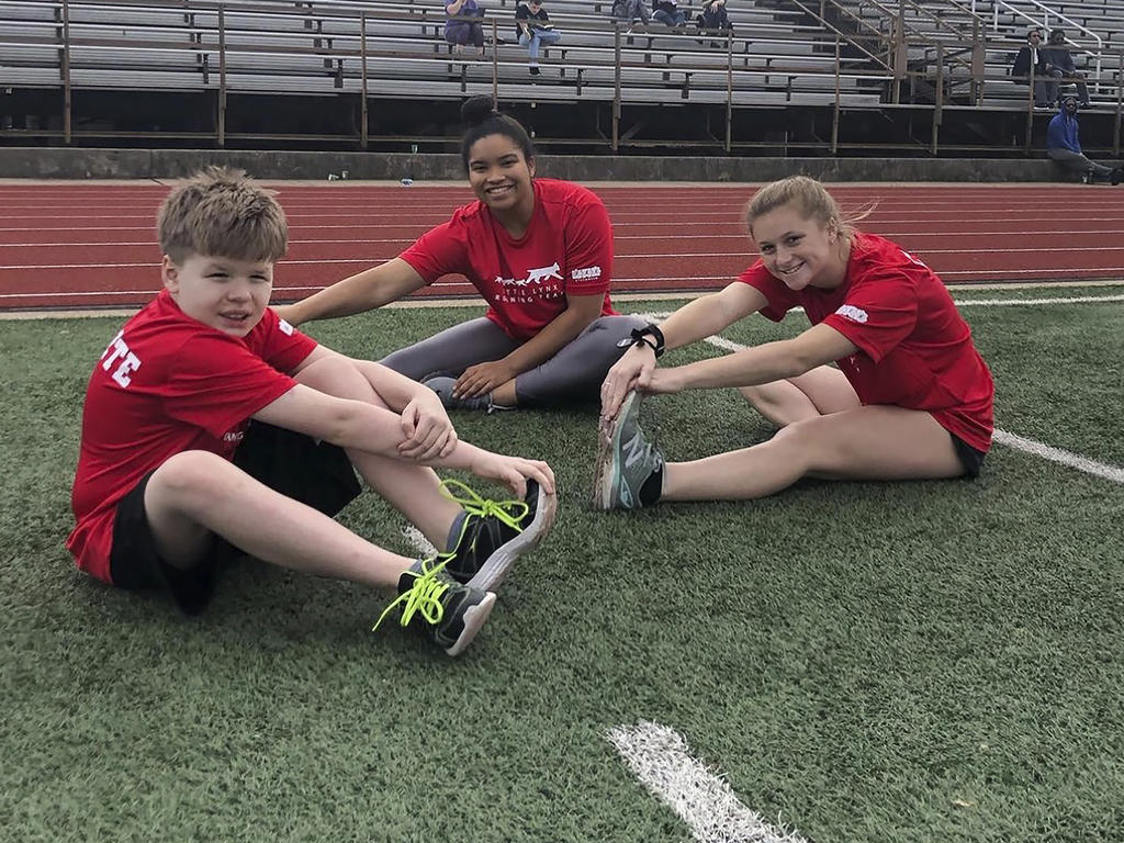 college students and a young boy stretch out on a track