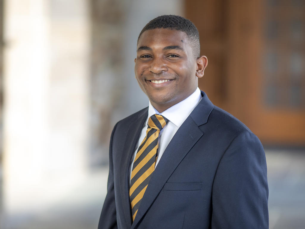 a young African American man in a suit and tie smiles at the camera