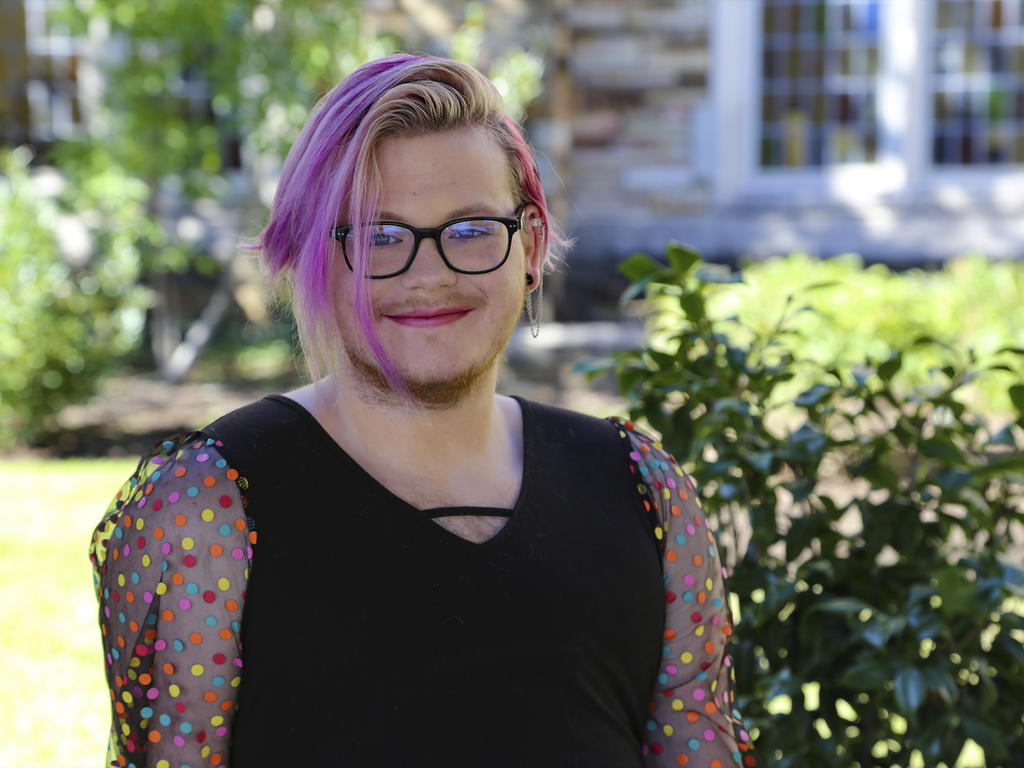 a student with pink hair and glasses smiles at the camera
