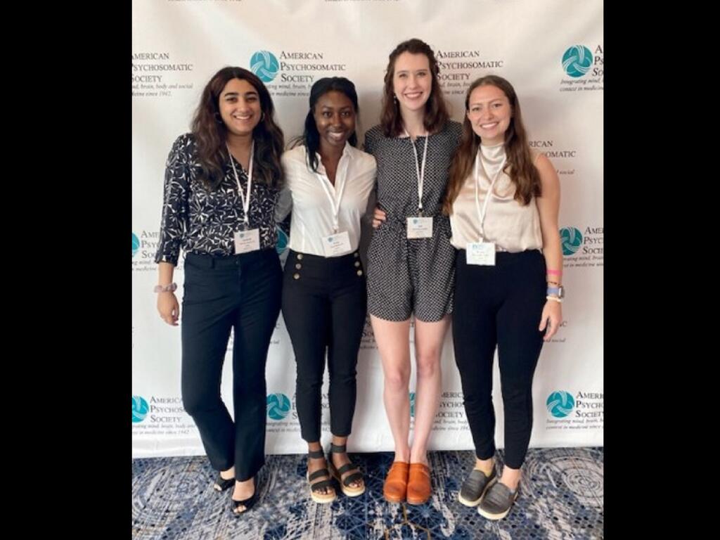 image of four Rhodes College students standing in front of a sign