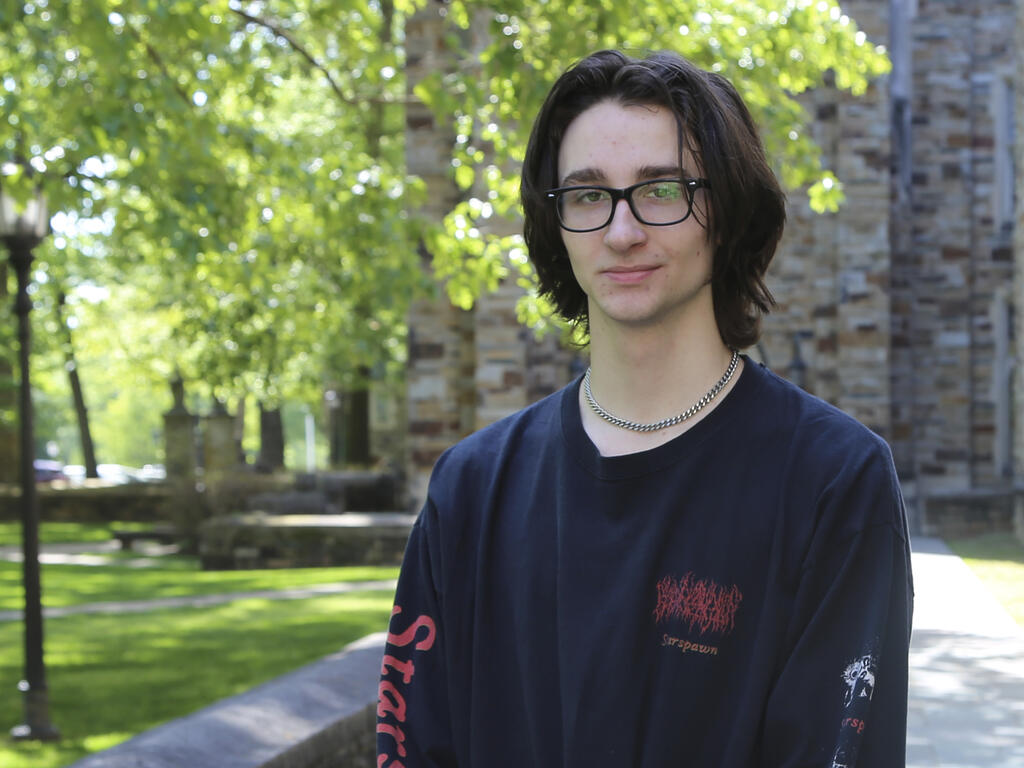 a young man with glasses and dark hair stands on campus