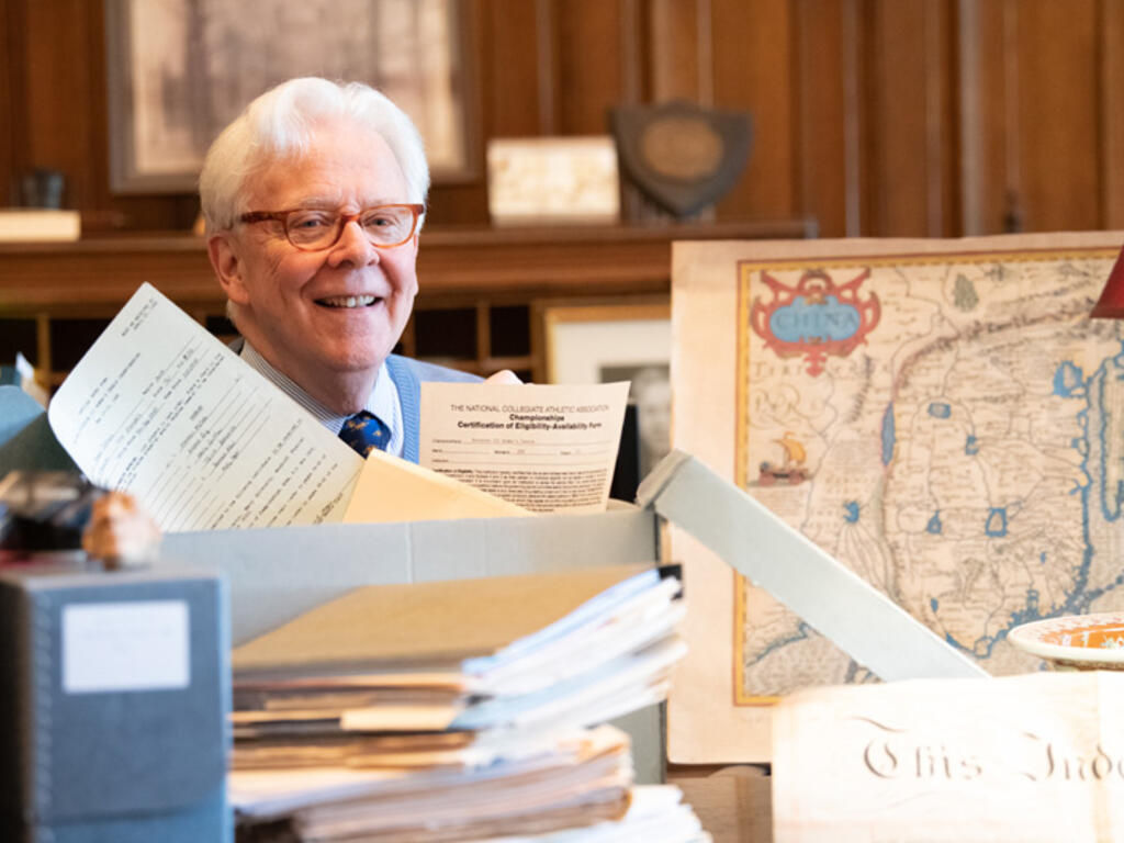 a dapper man with white hair surrounded by documents and maps