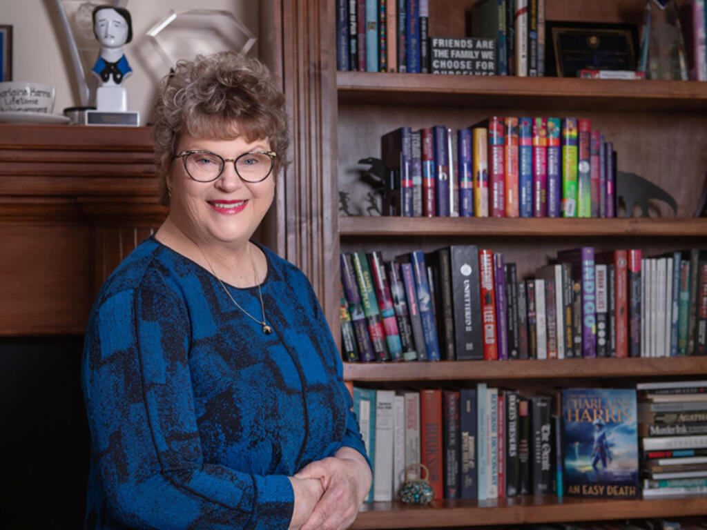 a woman in glasses stands next to a bookshelf