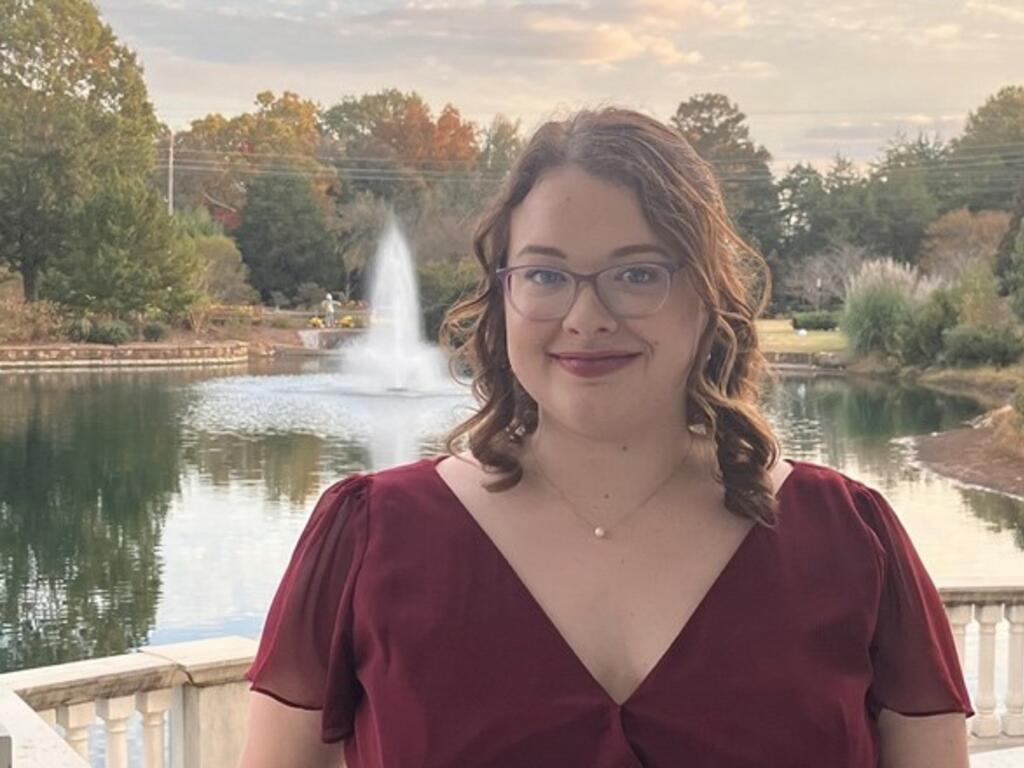 a young woman with glasses with a fountain in the background