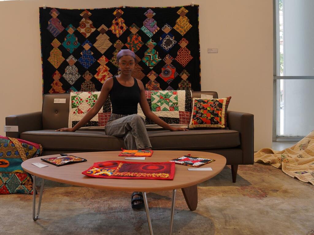 image of Janay Kelley sitting in front of a hanging quilt