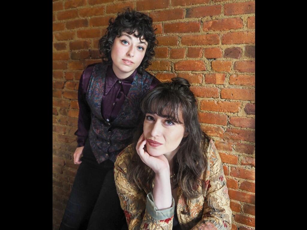 image of author duo in front of a brick wall
