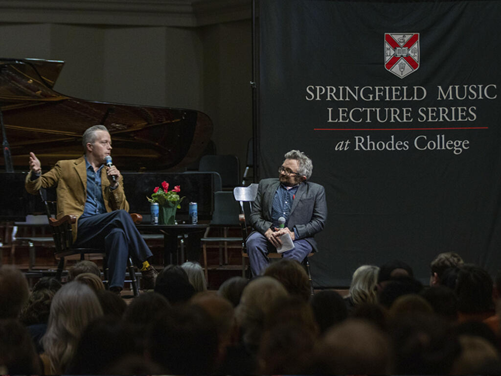 a man with a microphone talks with an interviewer on stage