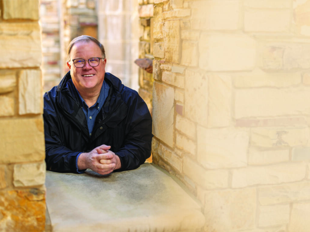 a man in glasses leans on the sill of a stone window