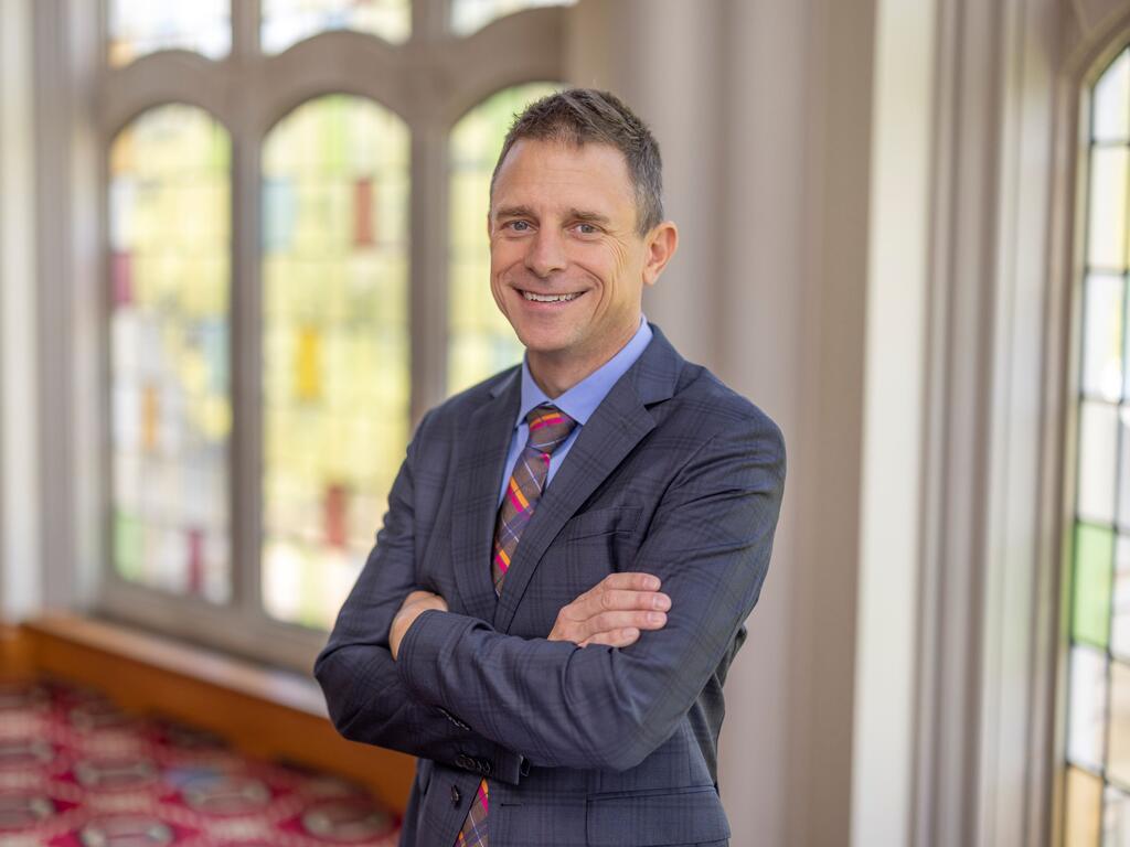 image of Scott Newstok standing in front or a stained glass window