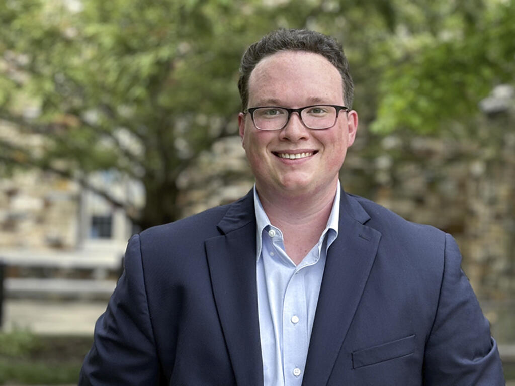 Ryan McTigue, a young man with glasses in a blue suit