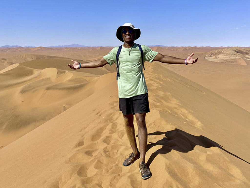 a young African American man smiles while standing on a sand dune in the desert