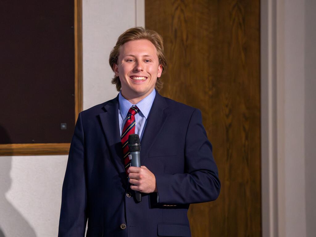 John Creveling dressed in a suit and tie, holding a microphone