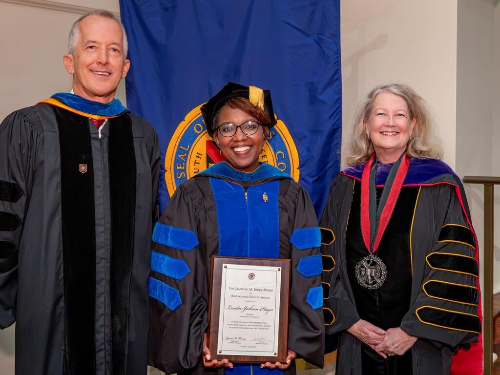 group image of Rhodes provost, professor holding plaque, and president