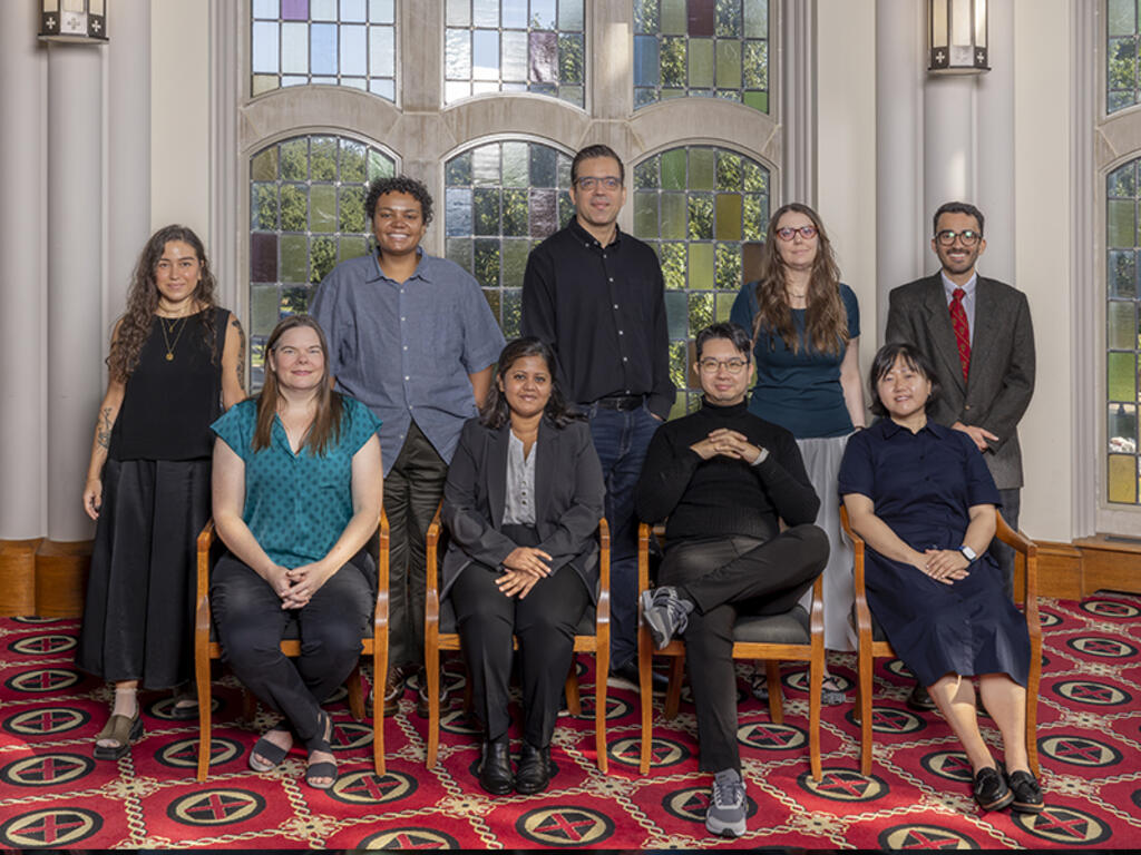 group image of Rhodes College faculty, standing and sitting in front of a stained glass window