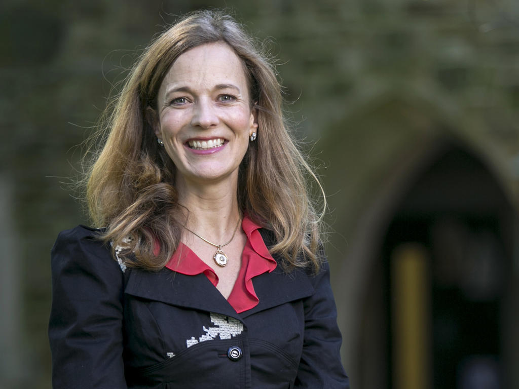 A female professor stands in front of a gothic arch.