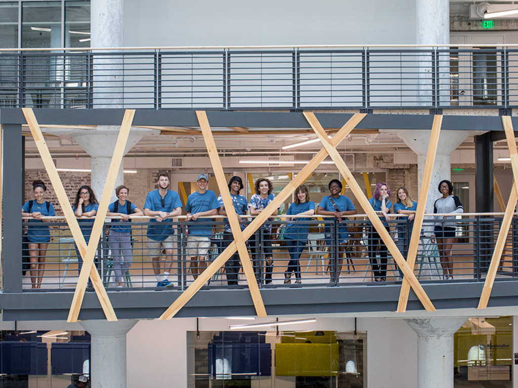 A group of diverse college students leaning against a second-story overhang balcony