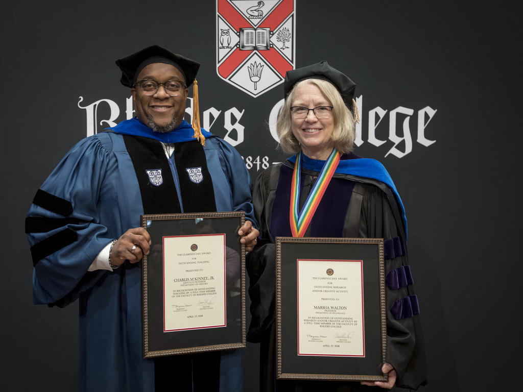 two professors dressed in academic robes hold award plaques