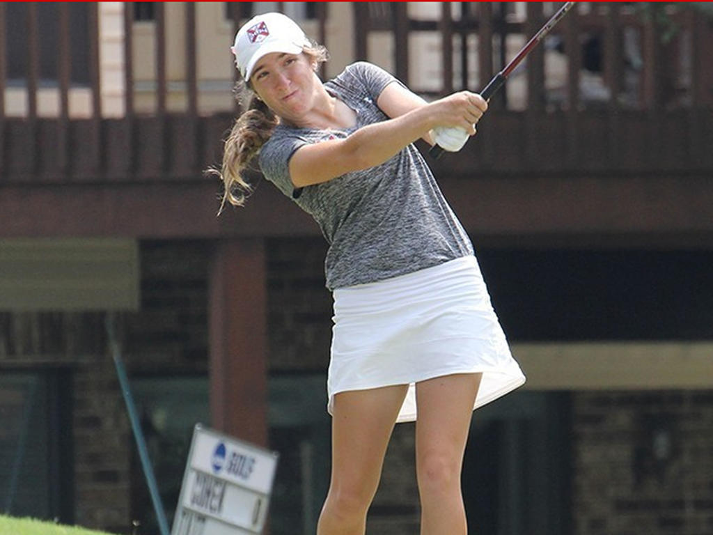 a young white woman focusing on hitting the golf ball in front of her