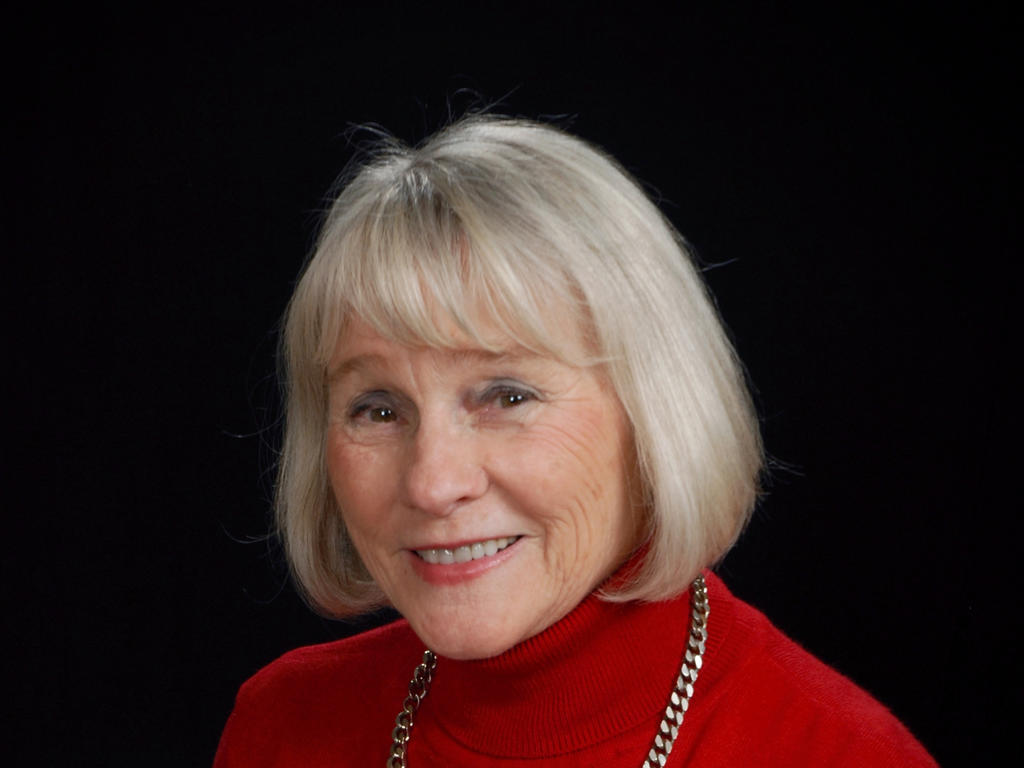 a headshot of an older woman standing in front of a black background