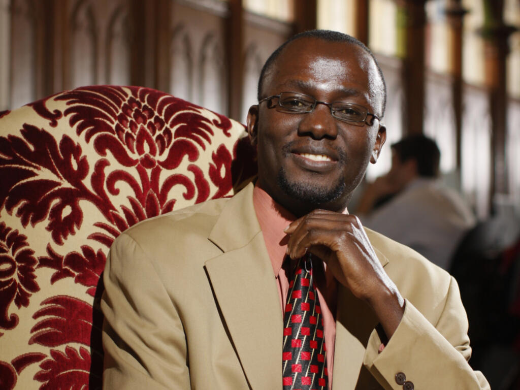 an african american man sitting and smiling in an ornately patterned red chair