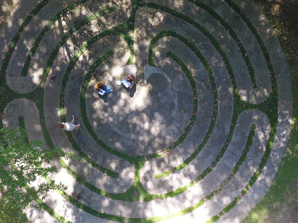 an aerial view of a stone labyrinth with students sitting within it