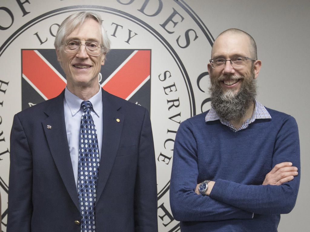 Two men, Professors David Rupke and Dr. John Mather, stand together in front of a wall featuring the Rhodes seal