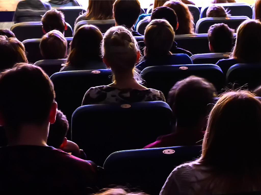 A view from the back of a dark room full of students seated