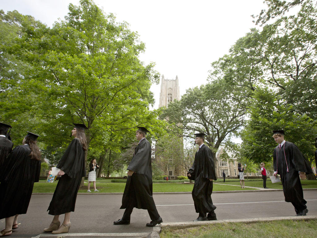 a line of college students doing the commencement march on campus