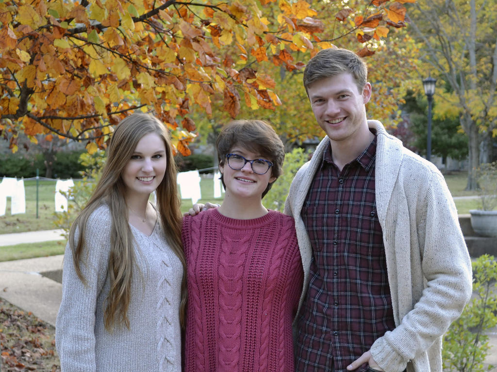 three young students smiling and standing near fall colored trees