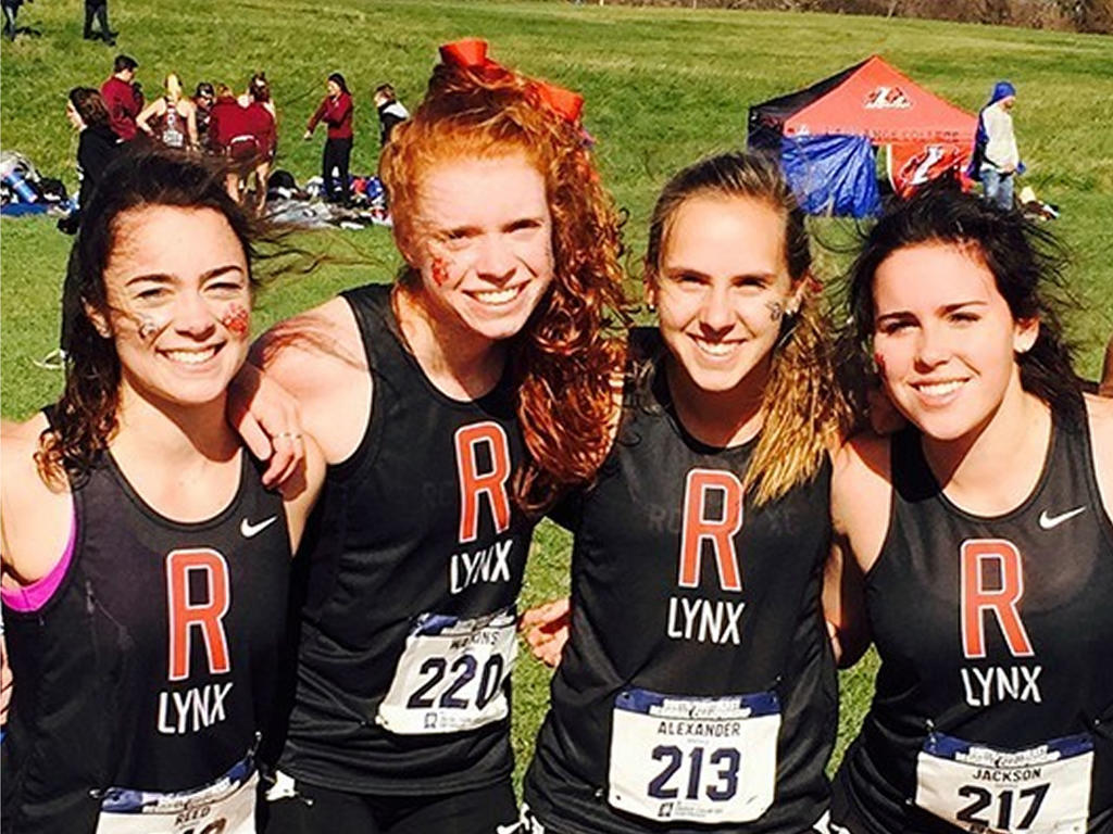 four white women smiling in their cross country uniforms on the track